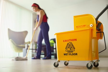 A commercial mop bucket and a professional janitor mopping tile floors.